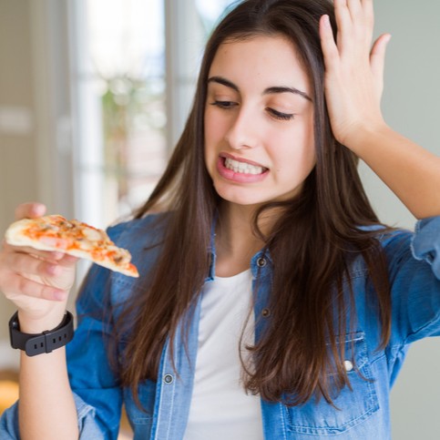 zakłopotana kobieta trzyma w ręku kawałek pizzy