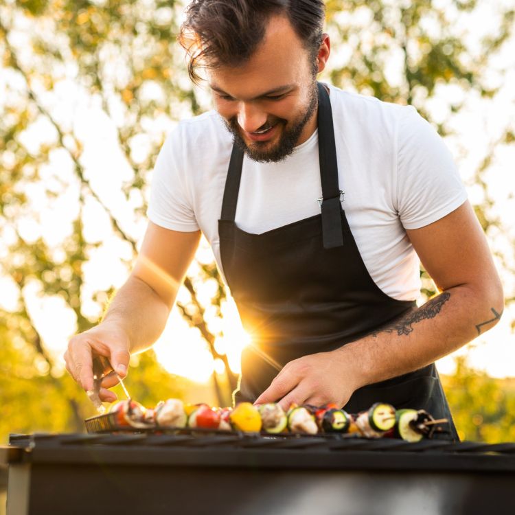 Osoba grilluje warzywne szaszłyki na zewnątrz.