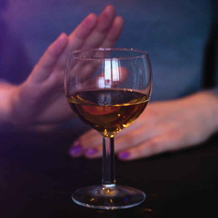 Osoba odmawia przyjęcia kieliszka z alkoholem, gestem dłoni odpychając go.