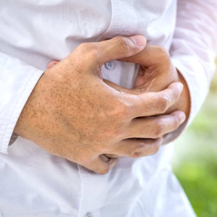 Zdjęcie przedstawia dłonie osoby w białej koszuli, splecione na wysokości brzucha w geście sugerującym ból lub dyskomfort.