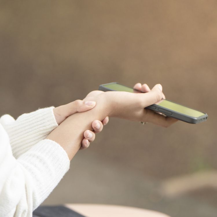 Zbliżenie na dłonie: jedna dłoń trzyma smartfon, druga obejmuje przedramię w okolicy nadgarstka.