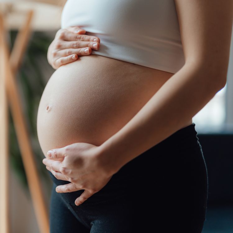 Widoczny brzuch kobiety w ciąży trzymany dłońmi – symbol zmian zachodzących w organizmie oraz nowego etapu w życiu.