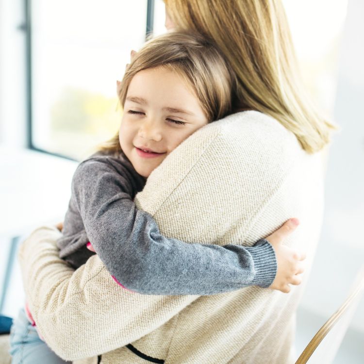 Uśmiechnięte dziecko z zamkniętymi oczami czule przytula się do osoby dorosłej. Widoczny jest bliski plan, podkreślający emocje, spokój i poczucie bezpieczeństwa