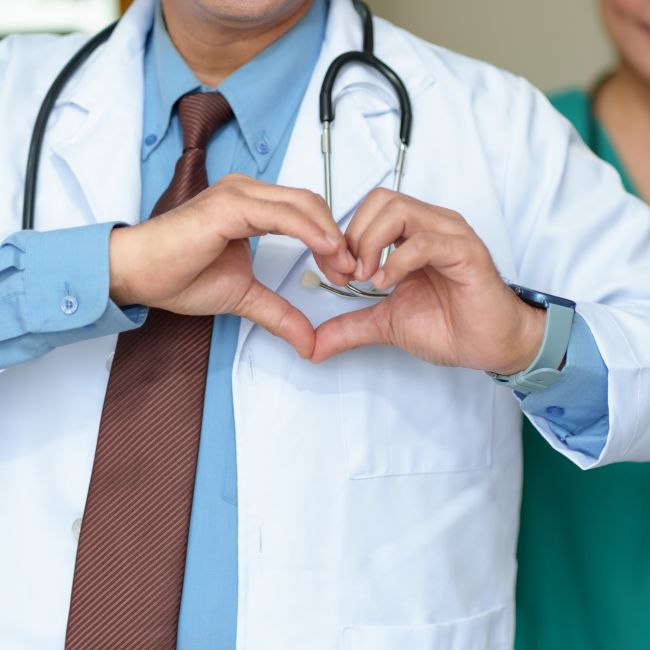 Osoba w białym fartuchu medycznym z widocznym stetoskopem, układająca dłonie w kształt serca – symbol profilaktyki chorób kardiologicznych i dbałości o zdrowie serca.
